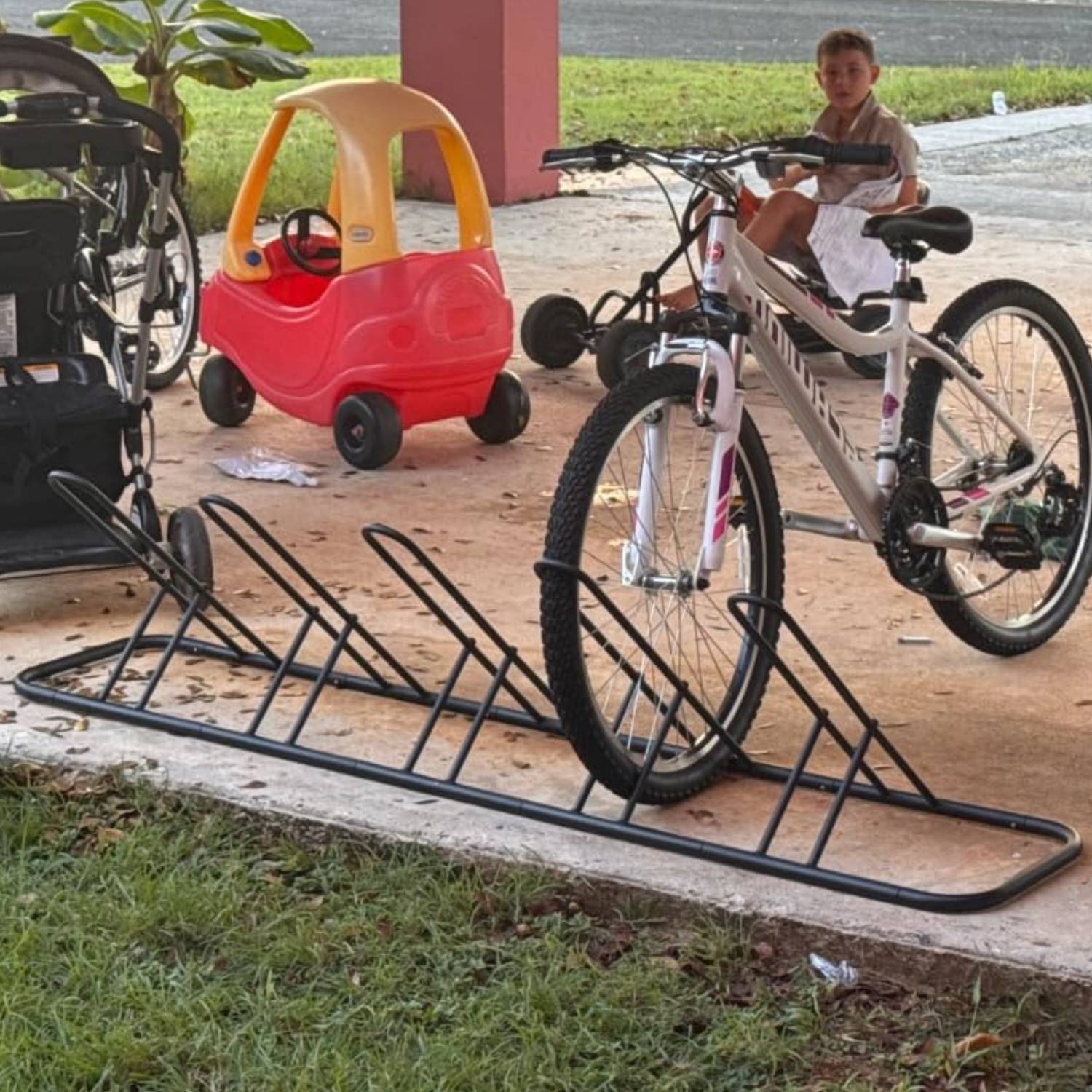 A child's bike parked in the floor rack on a concrete path outdoors
